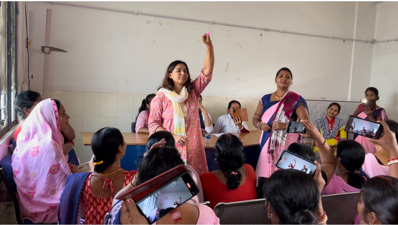 The MJWF founder holds up a menstrual cup during a community session, with women gathered around.