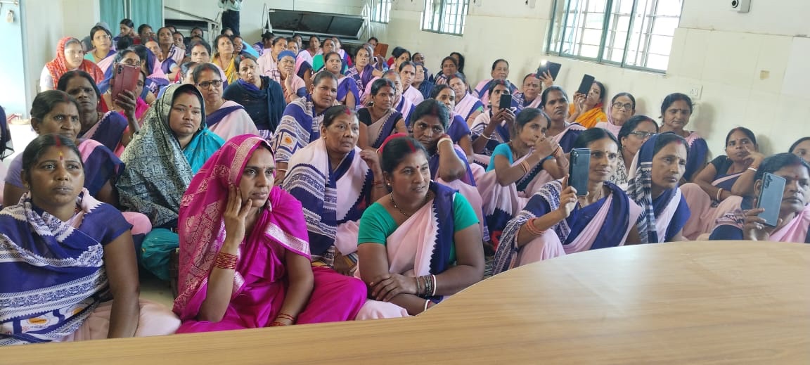 A hall full of women at an MJWF menstrual health awareness session, some filming on their phones.