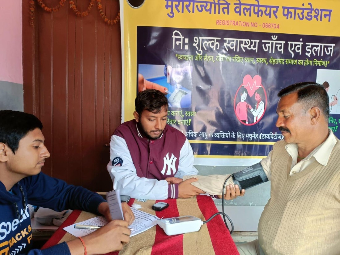 A young volunteer measures an older man's blood pressure at a free MJWF screening camp.