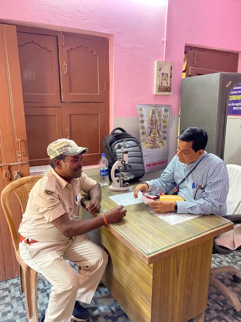 A man is seen by a doctor at the desk of a free MJWF health camp, with diagnostic equipment alongside.