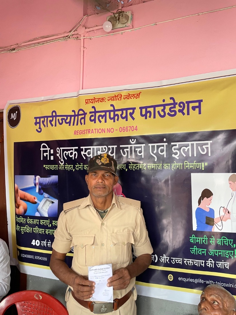 A man holds his free screening slip in front of the MJWF banner at a community health camp.